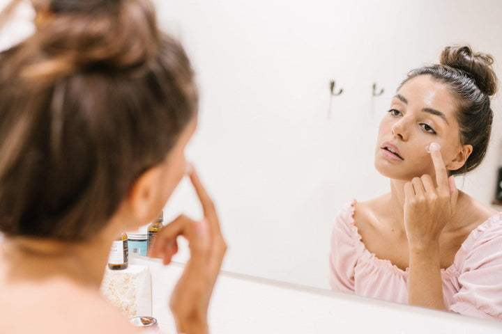 Een vrouw kijkt naar haar gezicht in de spiegel en brengt serum aan. Het Aloe vera retinol serum voedt en beschermt de huid tegen veroudering. Met avocado olie, retinol, bètacaroteen, collageen en arganolie.