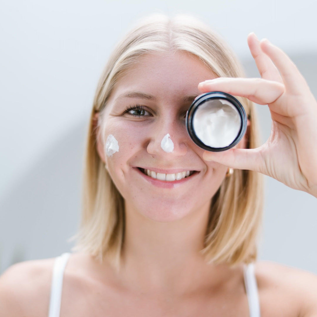 Een vrouw houdt een potje crème tegen haar oog, gebruikmakend van de hydraterende nachtcrème met hyaluronzuur & arganolie.