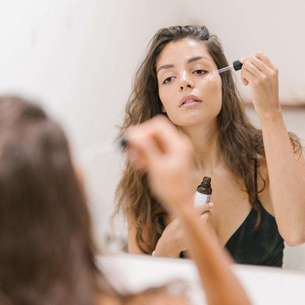 Een vrouw brengt oogdruppels aan voor de spiegel met Marula Olie Serum. Vermindert rimpels en zorgt voor een stralende huid.